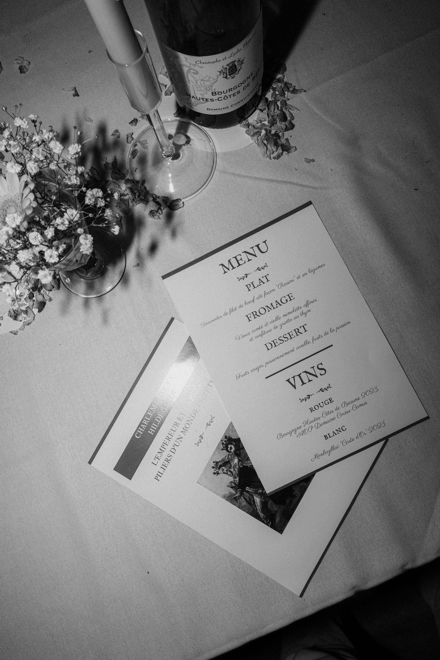 Black and white photo of elegant wedding menu cards with wine glasses and floral decorations.