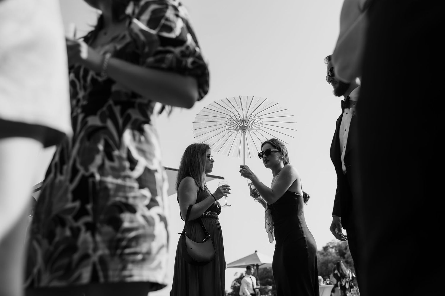 Black and white photo of guests with parasol at an outdoor celebration.
