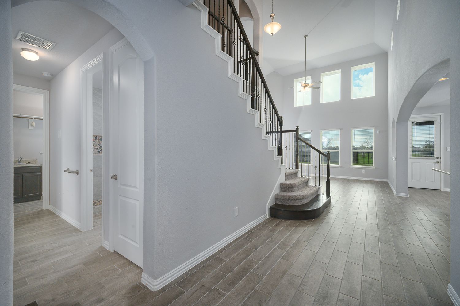 Modern interior hallway with white walls, recessed lighting, and wood flooring extending through multiple connected spaces in Rosharon Texas