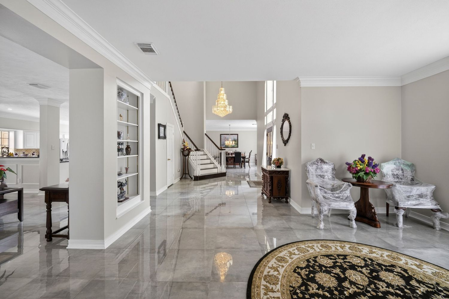 Elegant foyer with polished marble floors, crown molding, chandelier, staircase, and classic white and gray decor.