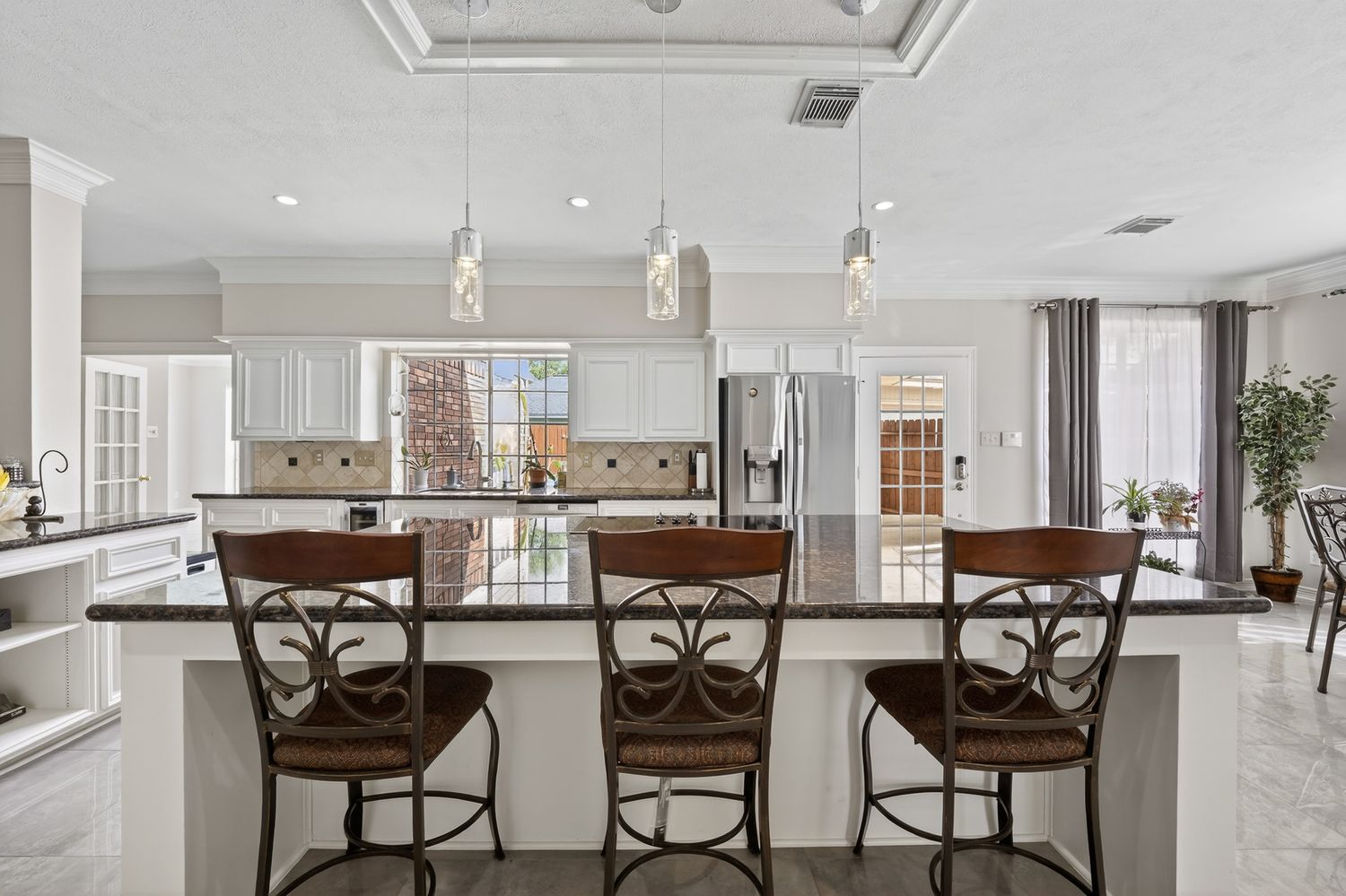 Elegant kitchen with dark granite island, pendant lights, white cabinets, and bar stools in a bright open layout.