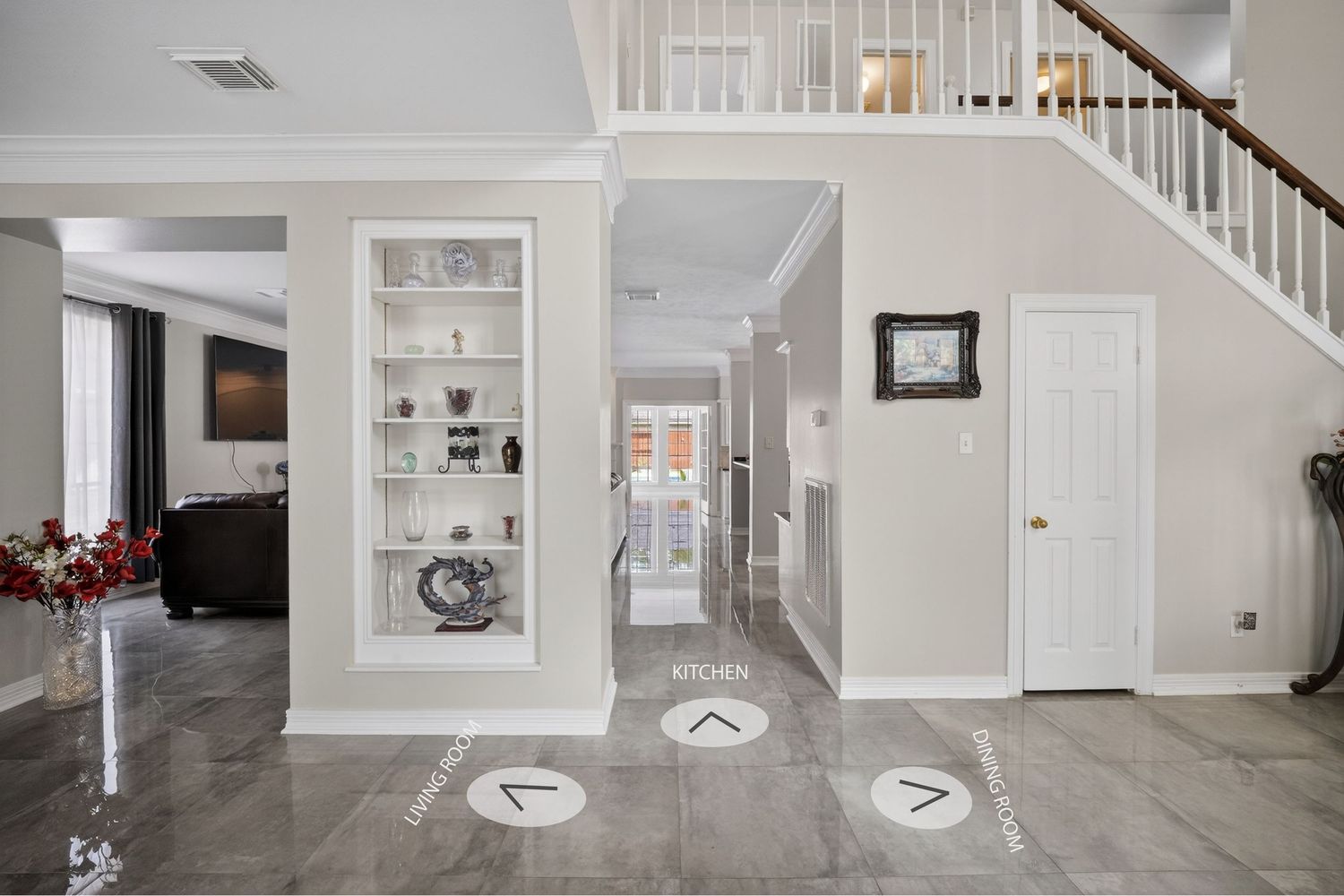 Elegant home entryway with marble floors, built-in shelving, white staircase, and open floor plan with directional markers.