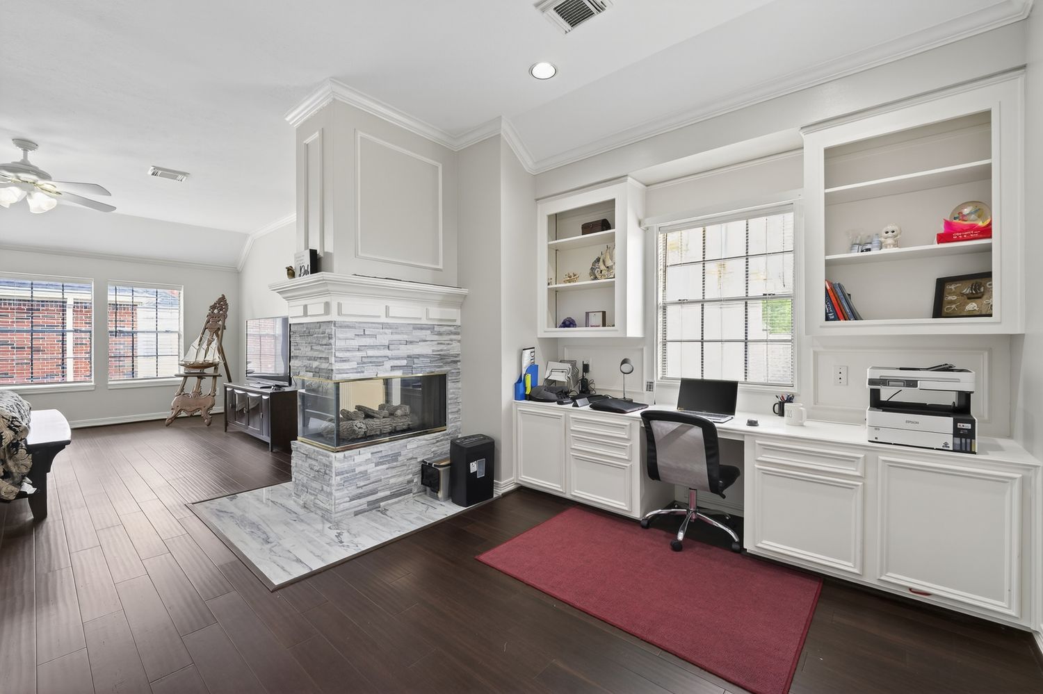 Home office with built-in white shelving, stone fireplace, dark hardwood floors, and a built-in desk with office chair.