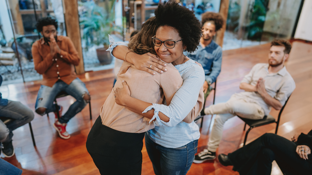 Women embracing during a group session, showing support, connection, and shared healing. Peers showing support.