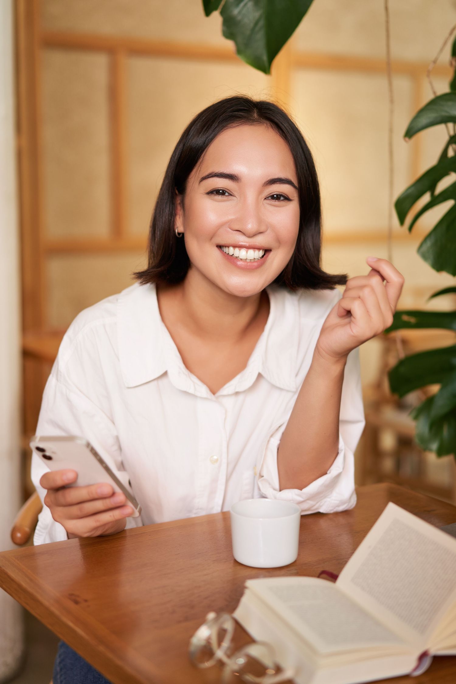 Woman smiling while holding her phone in a café, representing hope, connection, and positive life transitions.