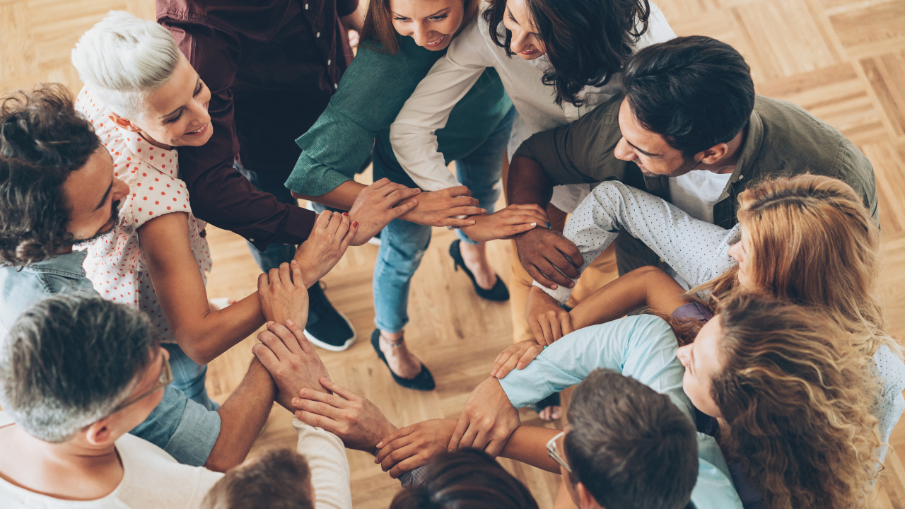 People standing in a circle holding hands, showing unity, support, and shared healing in a group session.