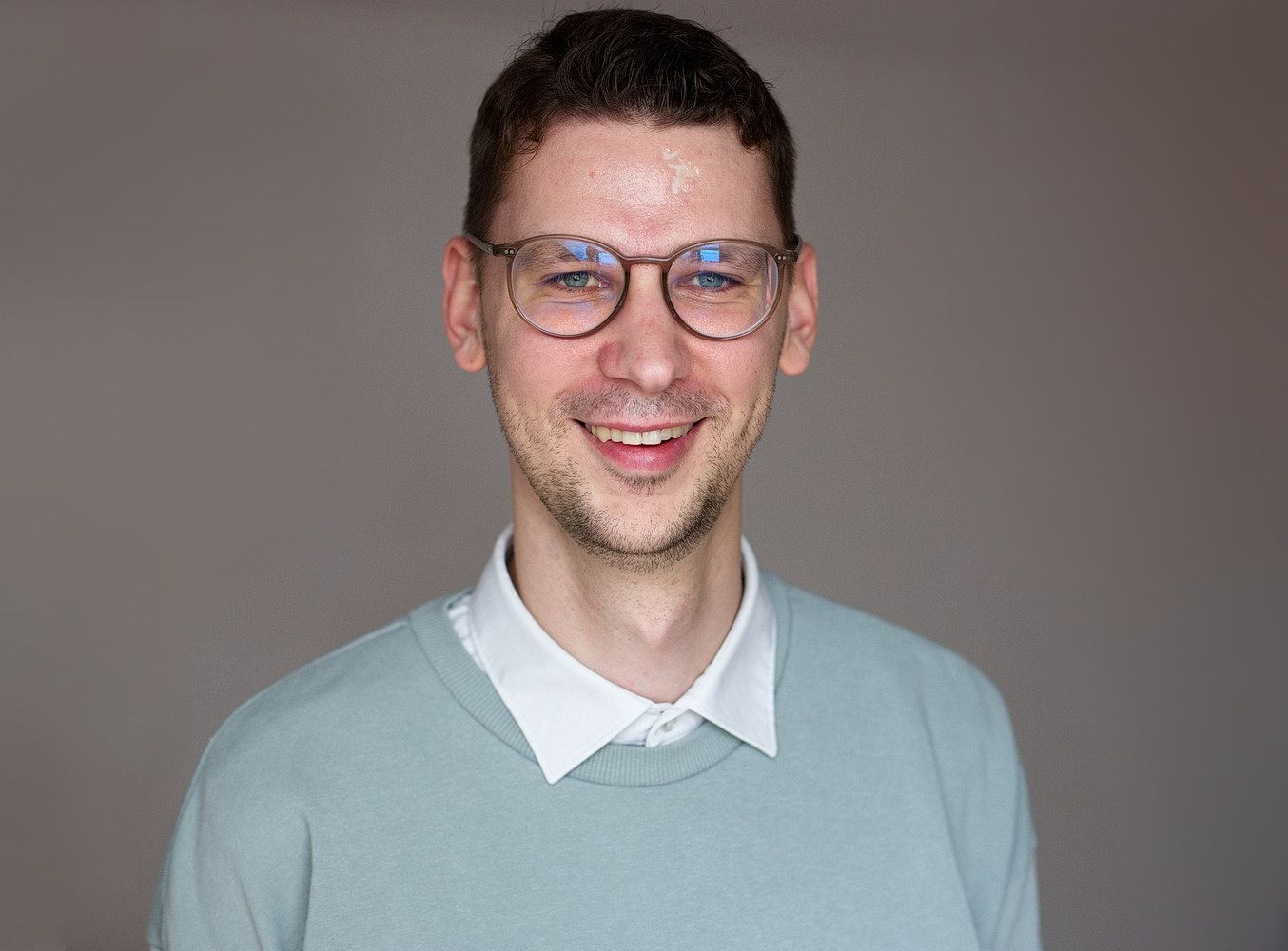 Ein Mann mit einem weißen Hemd und einem pastell-türkis-farbenem Pullover