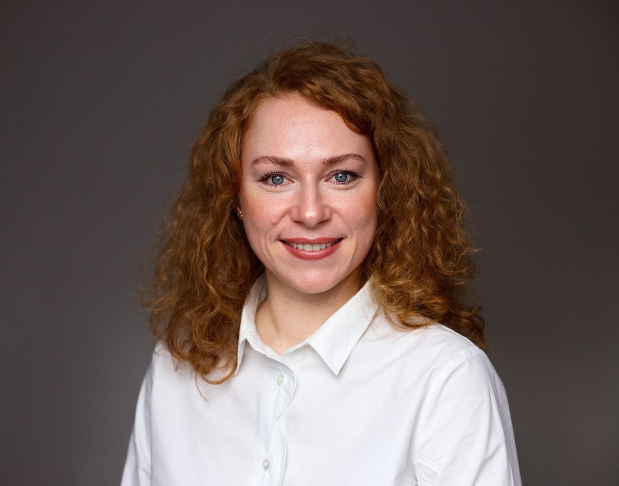 Bewerbungsbilder einer Frau mit lockigen roten Haaren in einer weißen Bluse vor einem dunklen Hintergrund