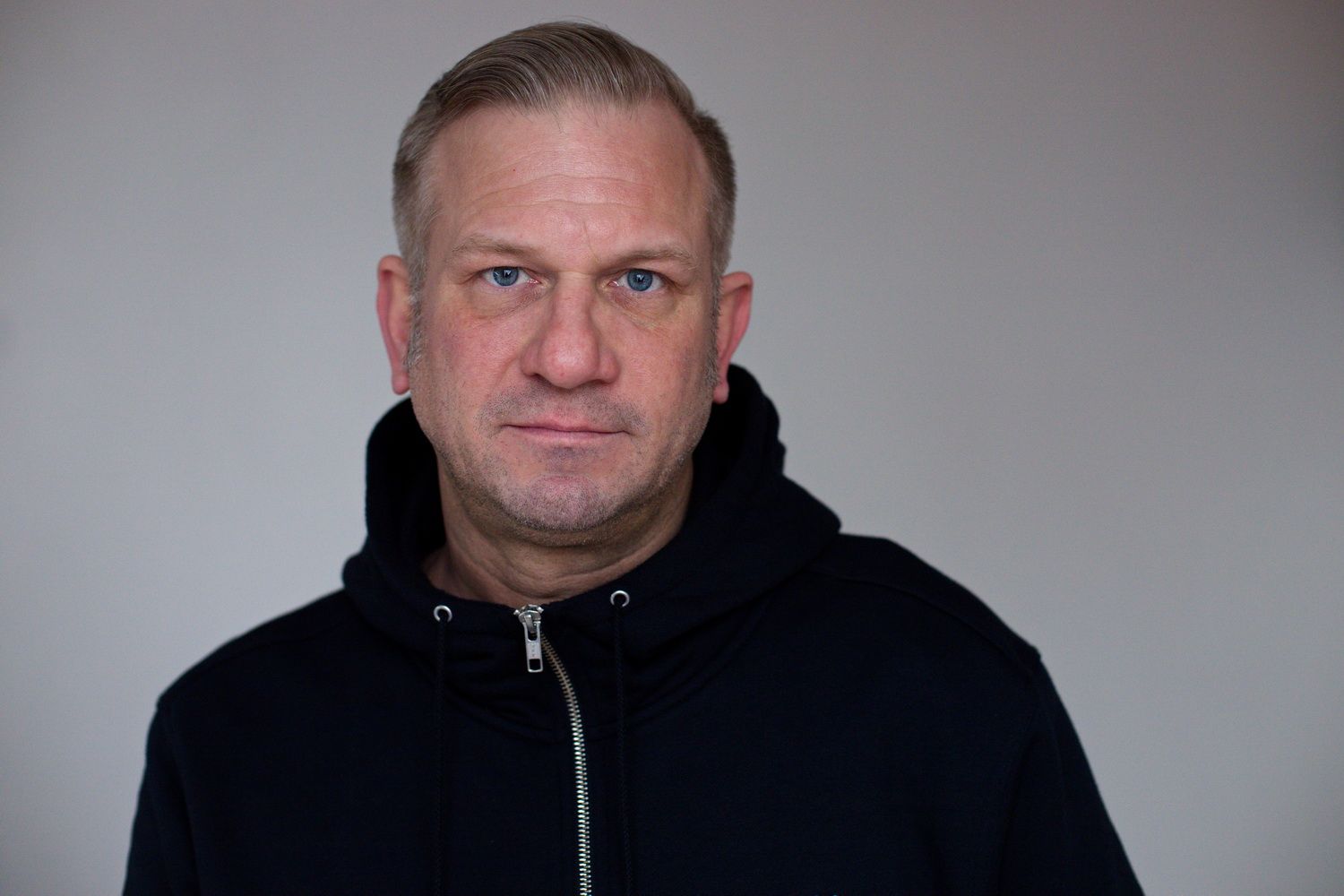Portrait eines Mannes im mittleren Alter in einem hoodie, mit einem neutralen Gesichtasudruck und Blick in die Kamera