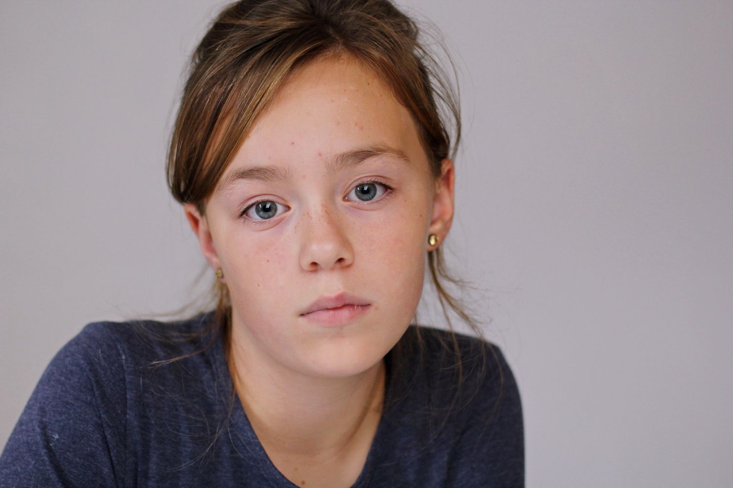 Portrait eines vorpubertären Mädchens, mit einem geneigten Kopf unt einem neutralen fast traurigen Blick in die Kamera