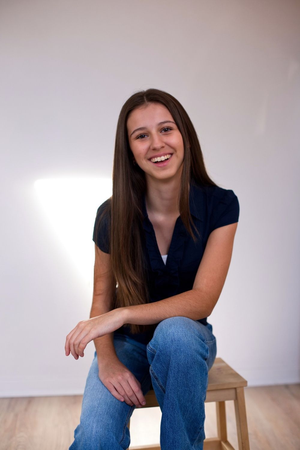 Ein Mädchen sitzt in einer lockeren Pose auf einem Hocker und lächelt in die Kamera, Studioportrait für eine Sedcard als Schauspielerin
