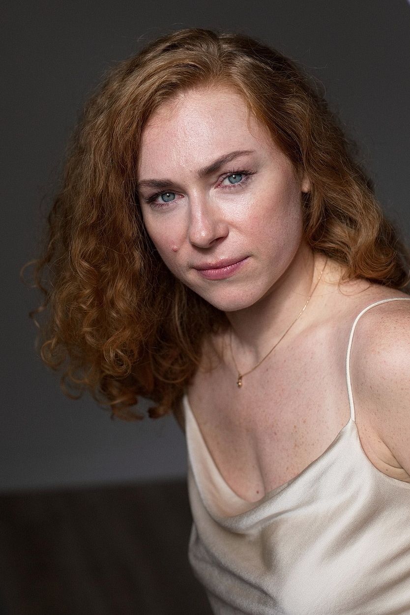 Portrait einer rothaarigen lockigen Frau die mit einem aussdrucksstarken Blick in die Kamera schaut
