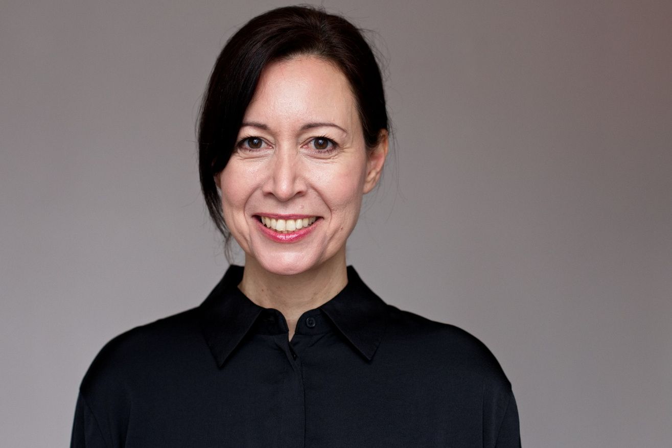 Portrait einer Frau mit geschlossenen Haaren und einer schwarzen Bluse.