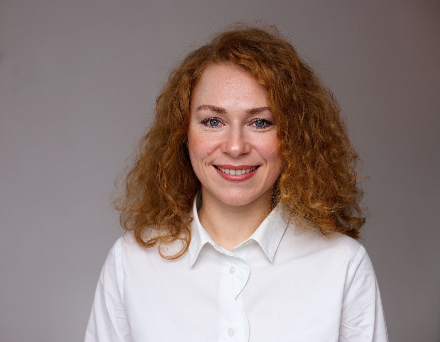Bewerbungsbilder einer Frau mit lockigen roten Haaren in einer weißen Bluse vor einem dunklen Hintergrund