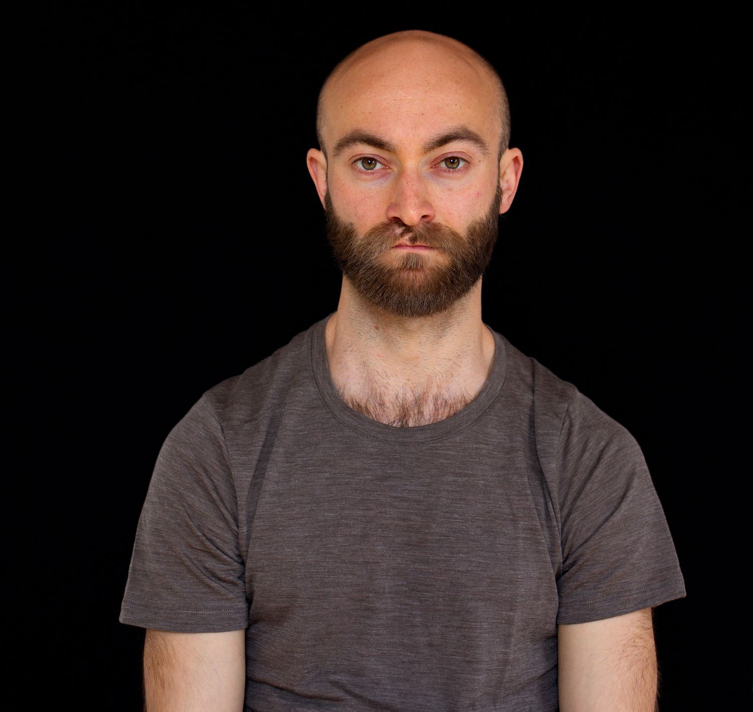 Portrait eines jungen bärtigen und glatzköpfigen Mannes mit einem neutralen fast traurigen Blick in die Kamera
