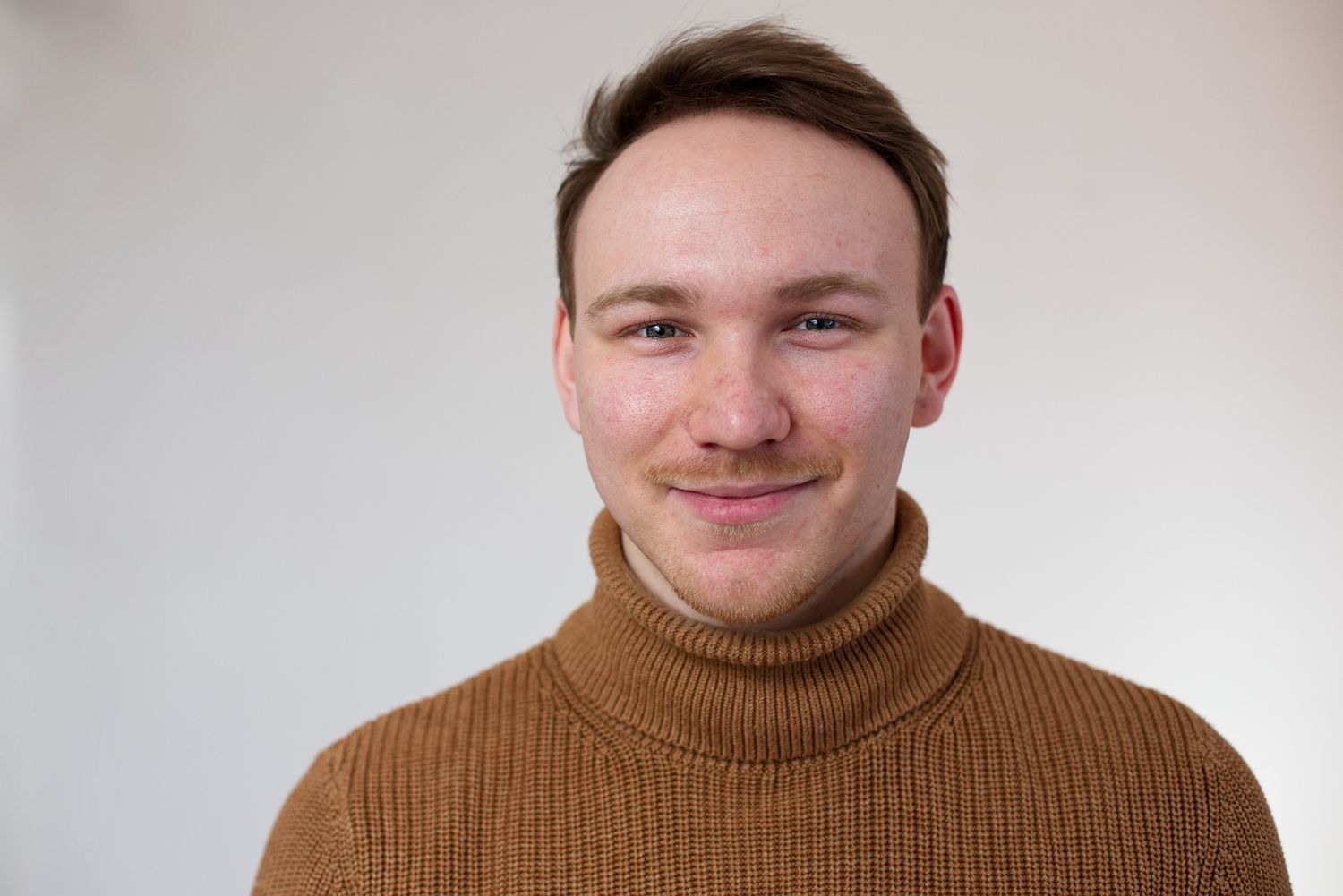 Ein Mann mit einem erdfarbenem Rollkragenpullover, passend zu seiner Bart- und Haarfarbe