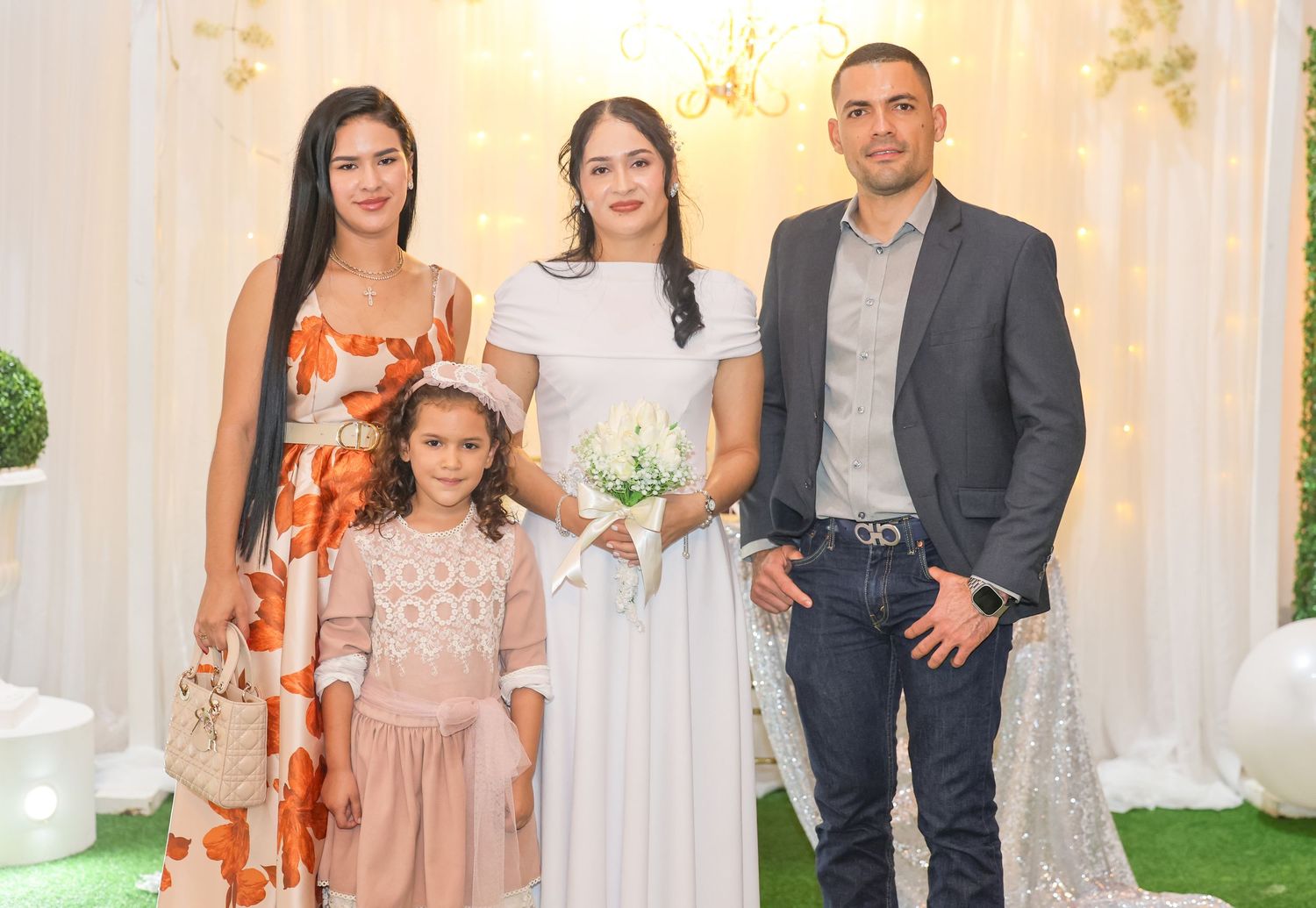 Family of four poses together at elegant white wedding reception venue with floral decorations.