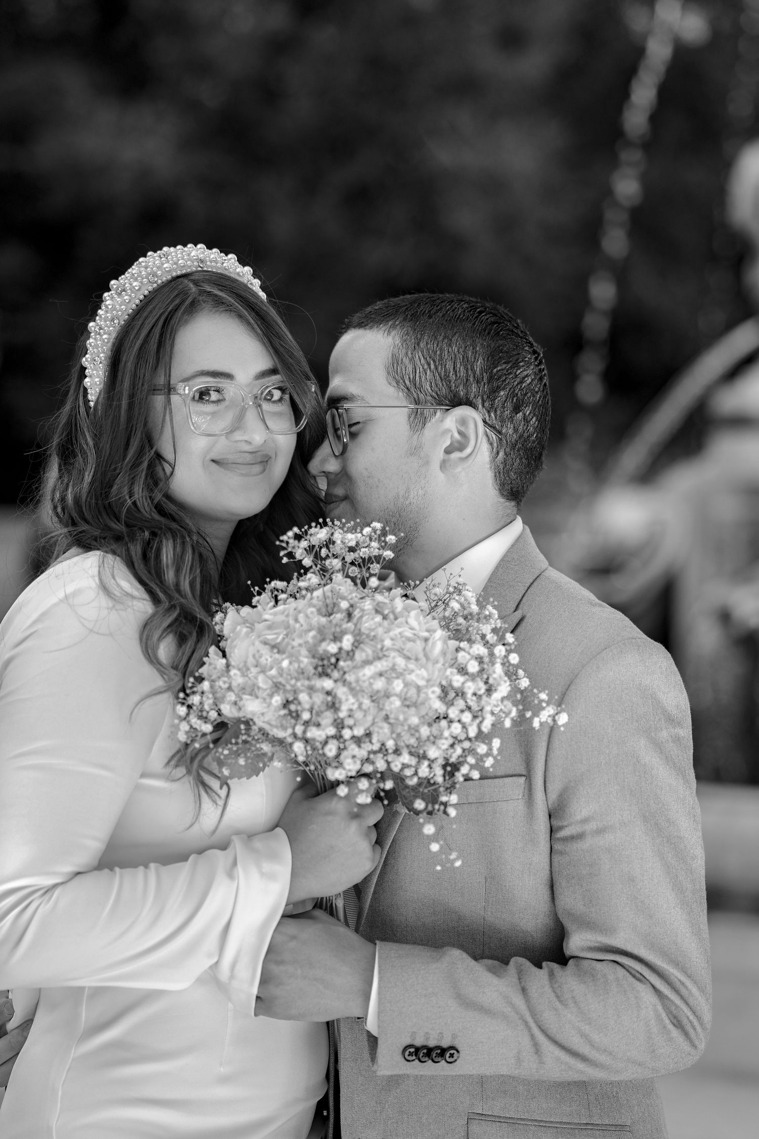 Black and white wedding portrait of a smiling bride and groom holding a bouquet of baby's breath flowers.