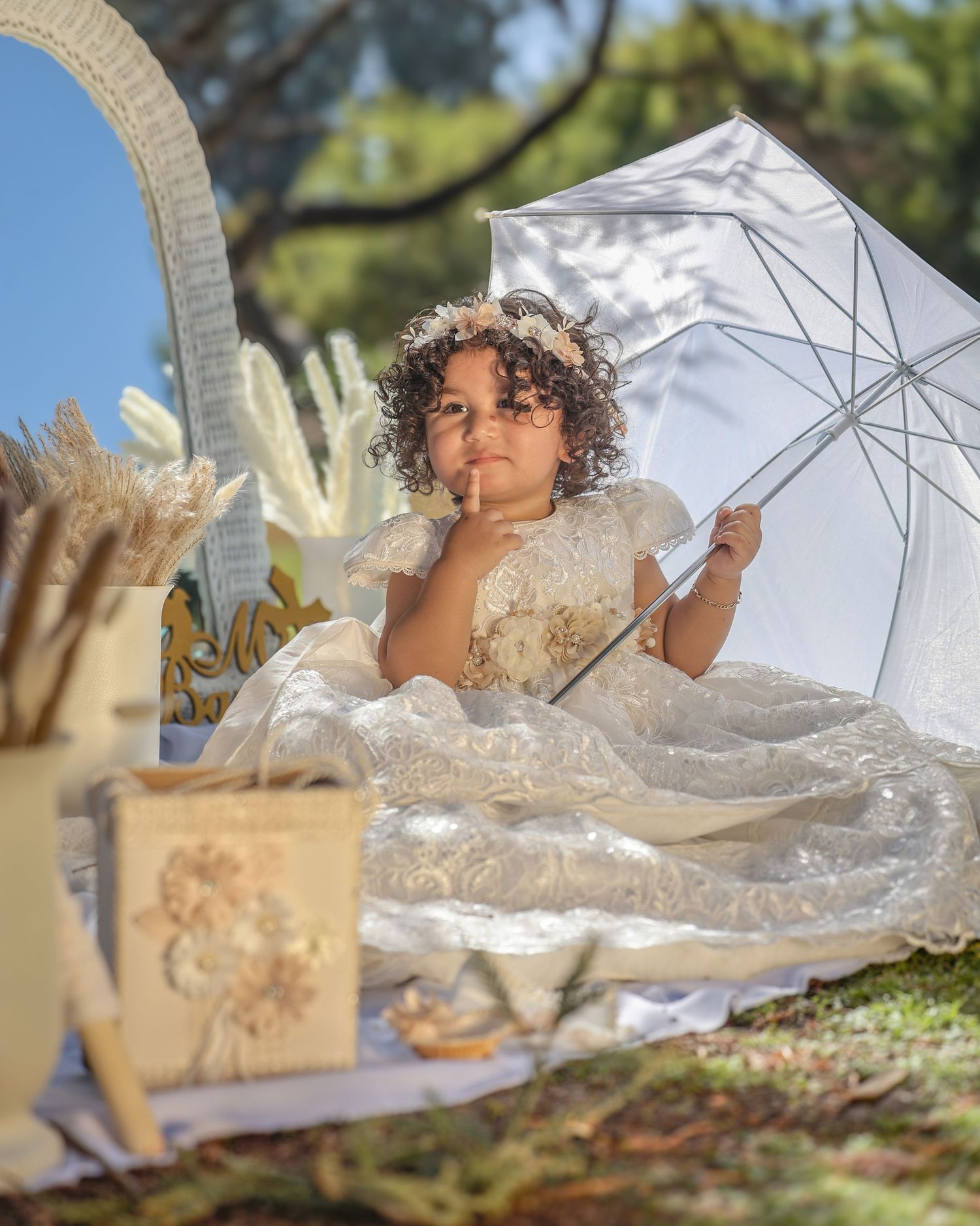 Child in white dress poses with parasol during outdoor photoshoot.