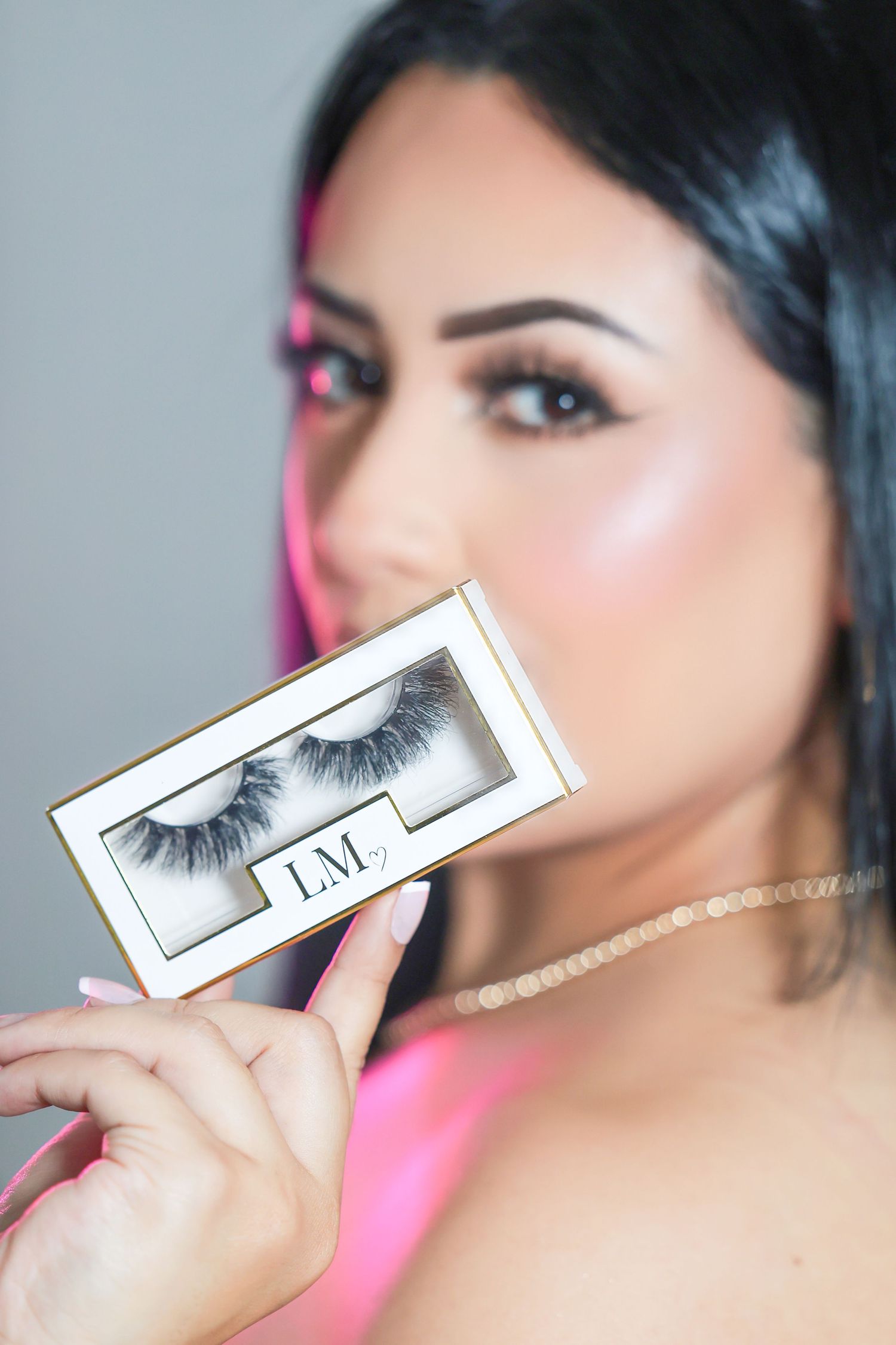 Woman holding LM brand false eyelashes box close to her face with glamorous makeup look.