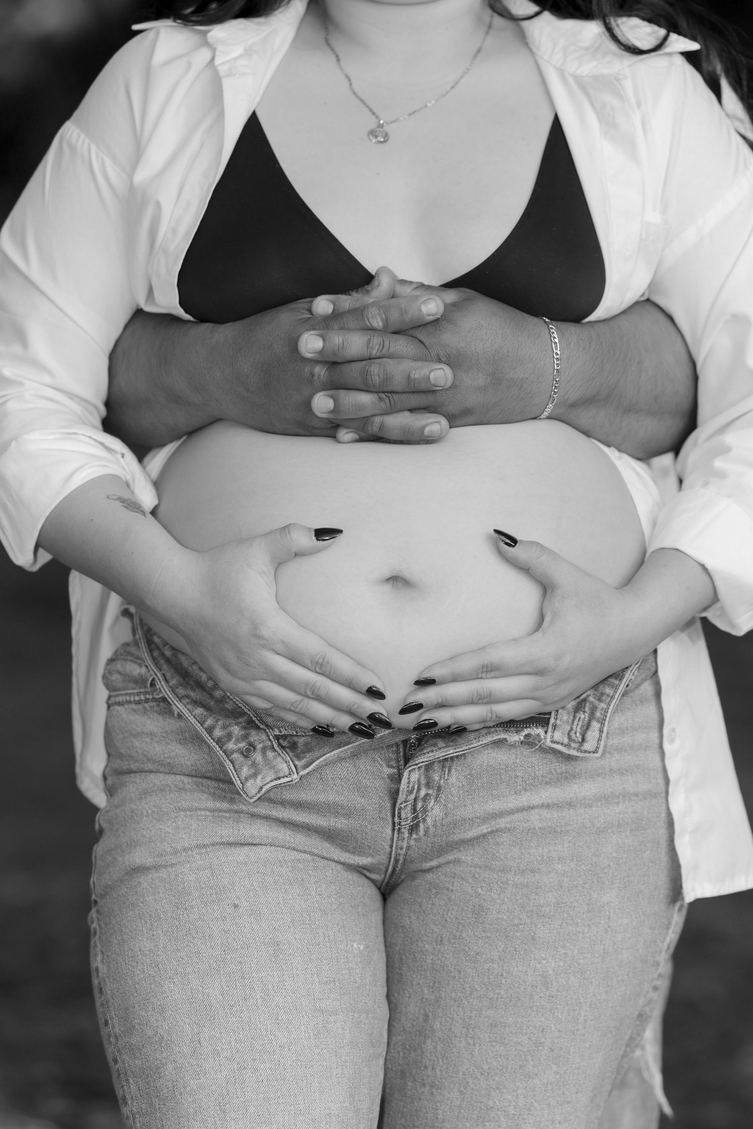 Black and white close-up of couple cradling pregnant belly outdoors, maternity photo.