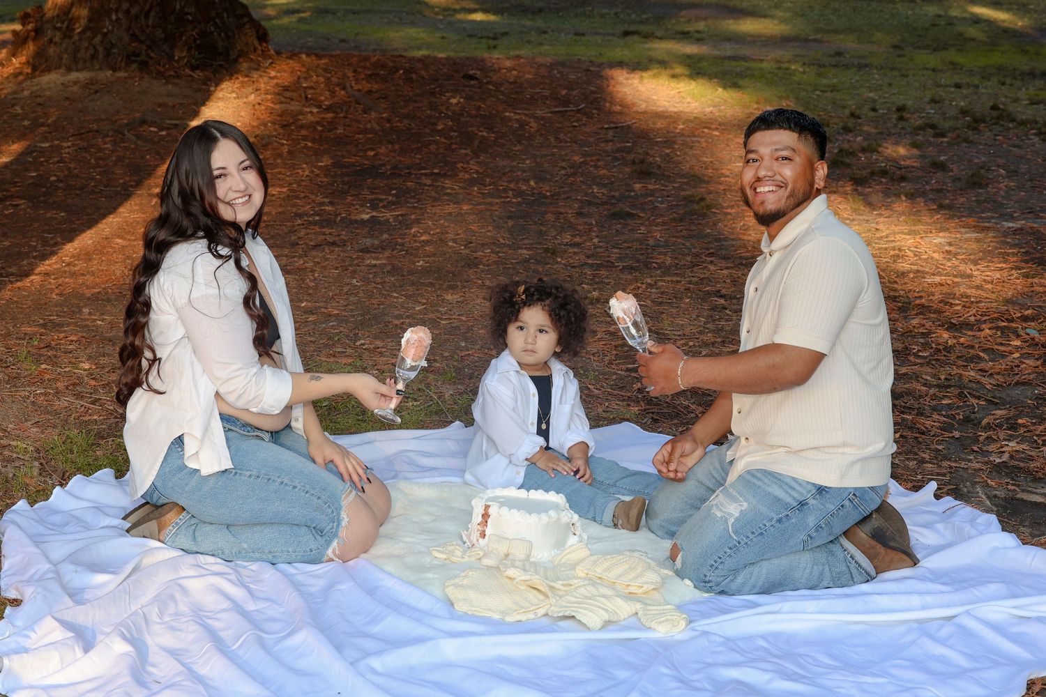 Family enjoys picnic together on blanket in wooded setting.