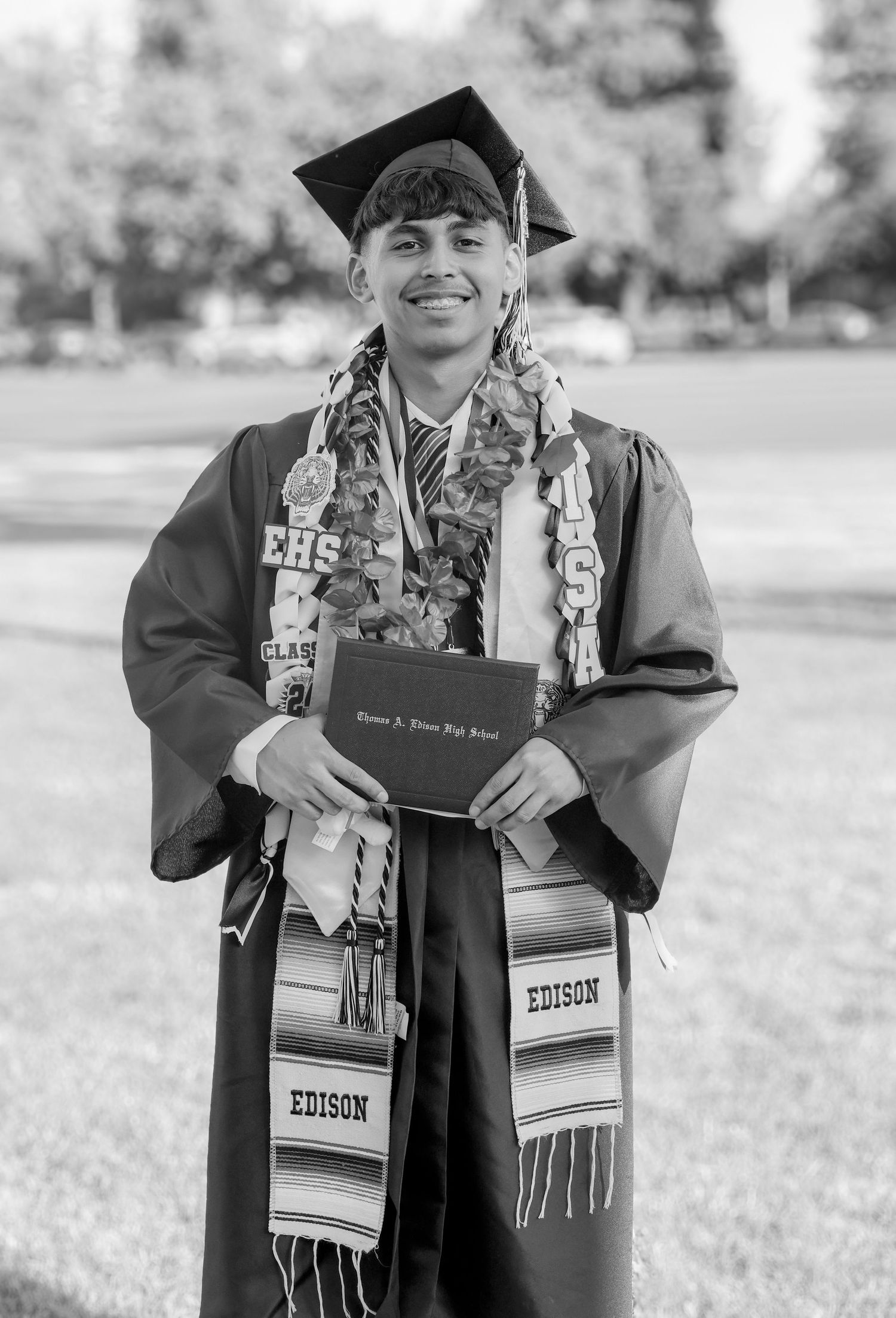 Black and white graduation photo of smiling male student in cap and gown holding diploma.