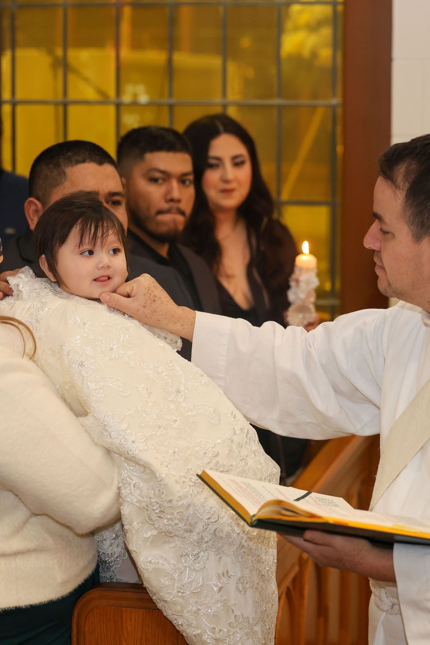 Priest performing baptism ceremony on young child in white gown inside a church.