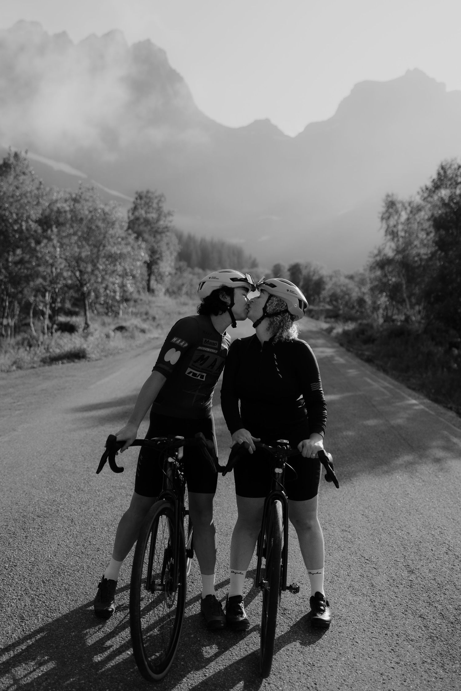 Cyclists with bikes silhouetted against a mountain landscape in black and white.