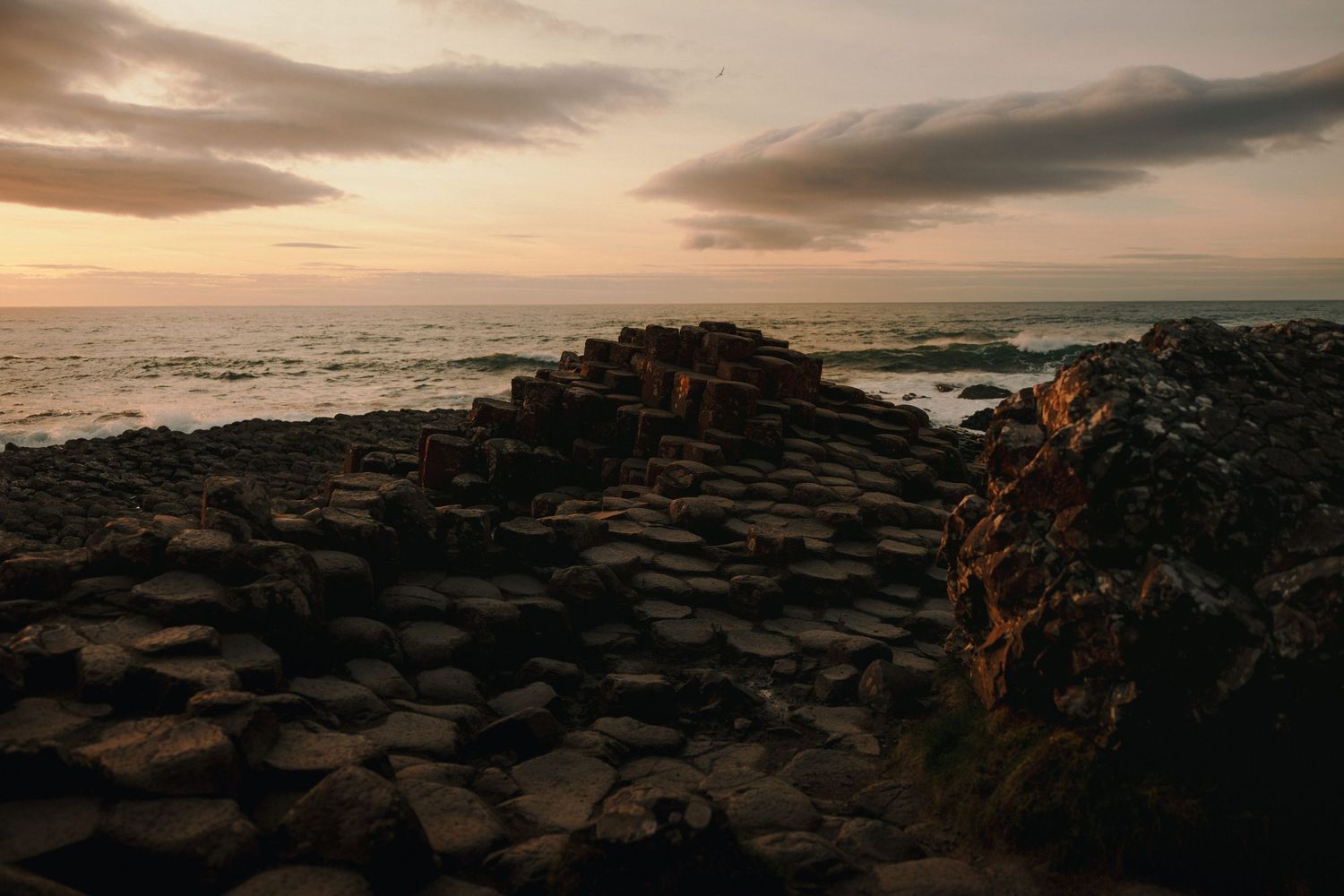 Sunset illuminates rocky coastal landscape at Giant's Causeway with hexagonal basalt formations.