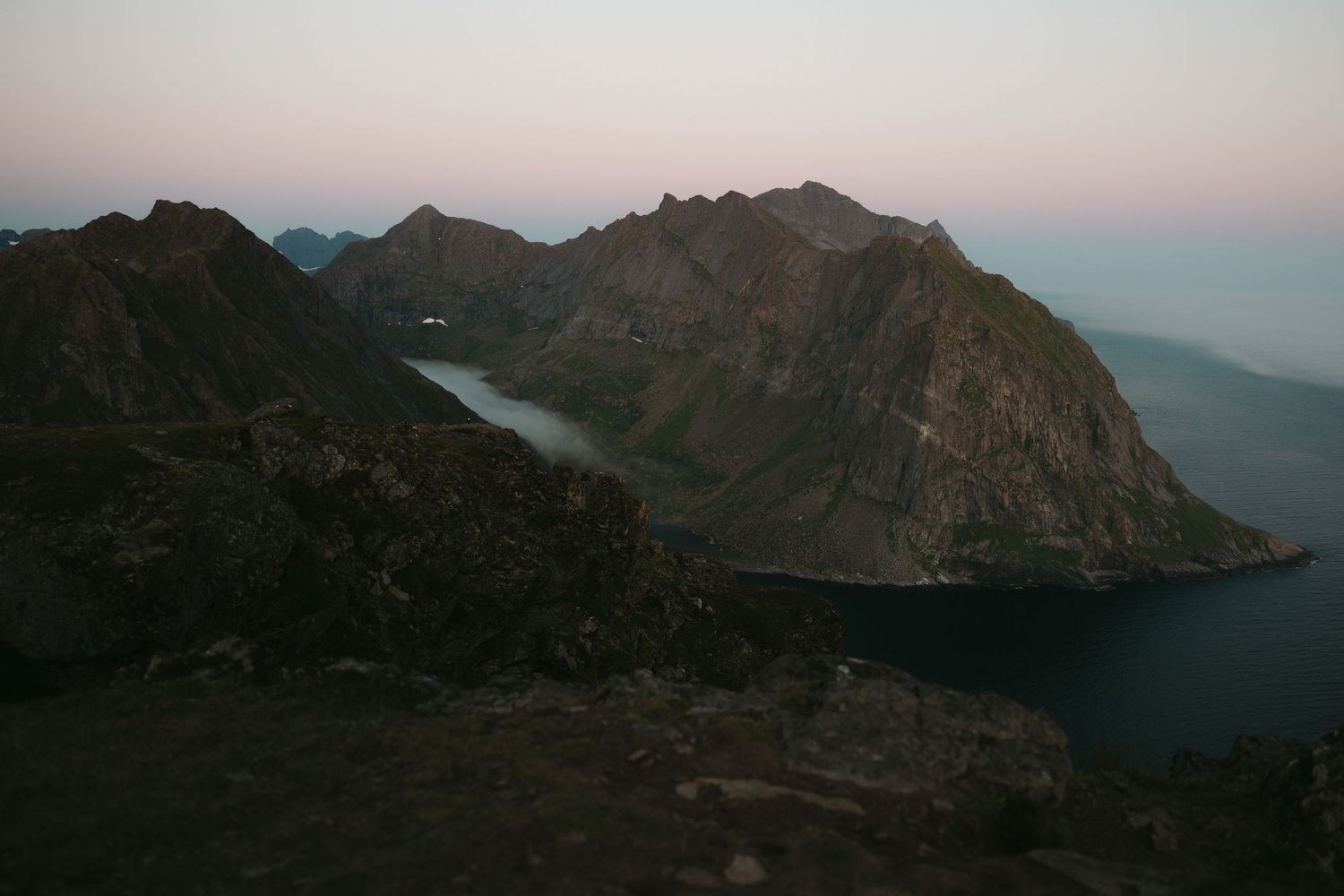 Dramatic mountain landscape at dusk with a lake nestled between rugged peaks.