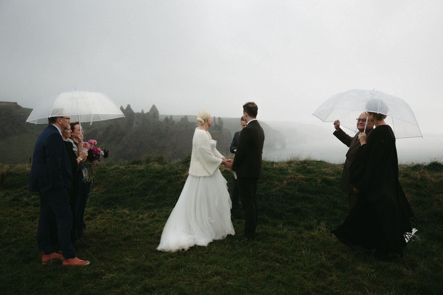 A misty outdoor wedding photoshoot with white umbrellas and silhouettes against a moody mountain landscape.