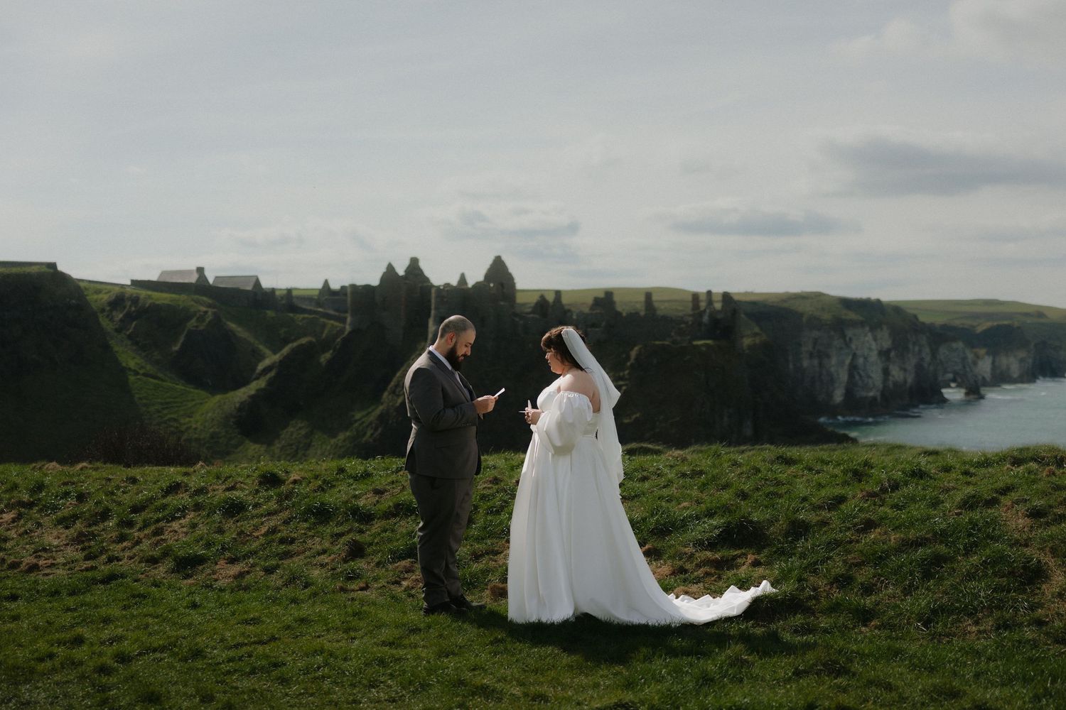 Bride and groom exchange vows on dramatic Irish coastal cliffs with white chalk rocks and green headlands backdrop.