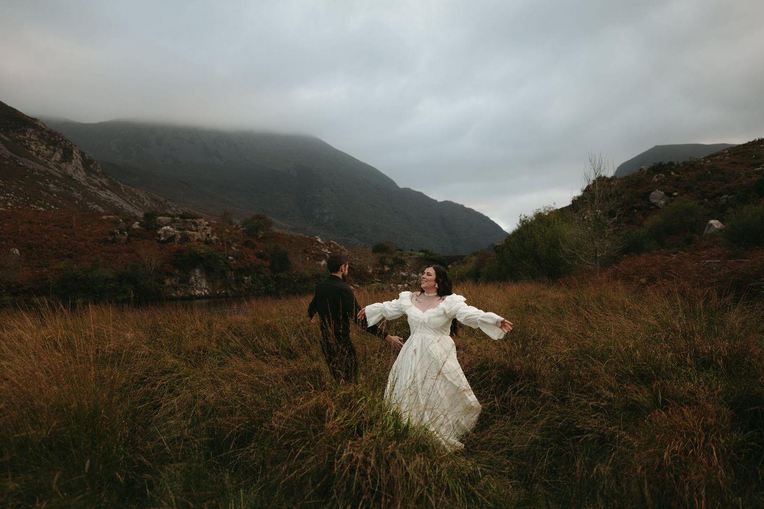 A dramatic wedding portrait overlooking misty mountain lakes at dusk in Killarney, Ireland.