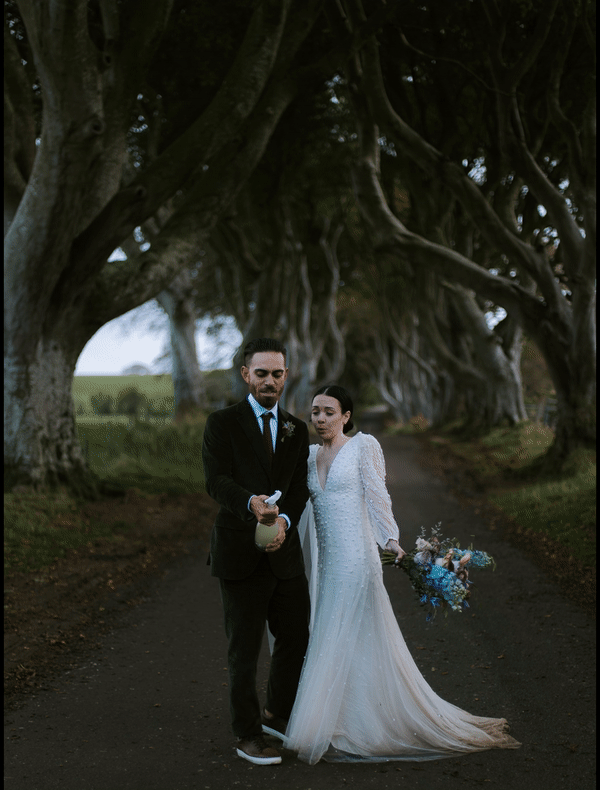A couple celebrates by popping champagne at the dark hedges