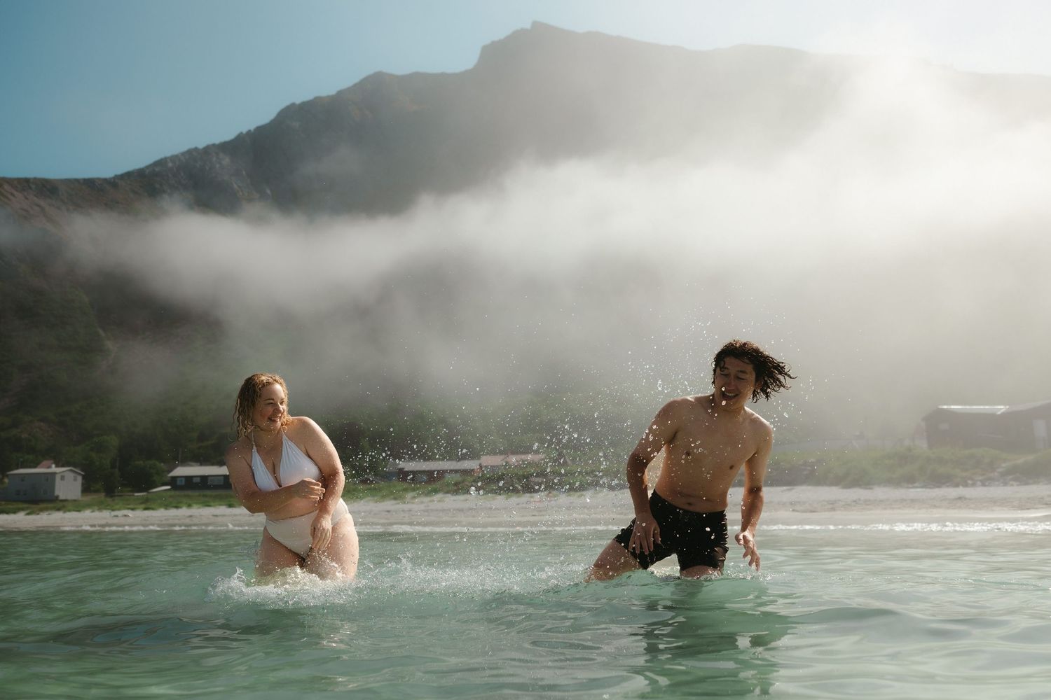 Scenic beach swimming scene with misty mountains and waves in the background.