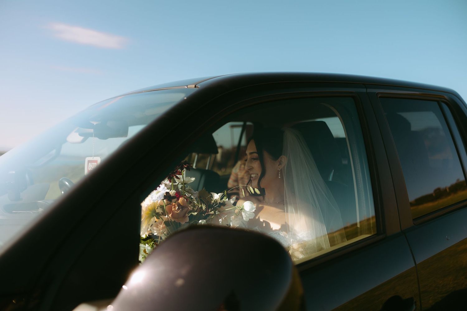 A black car drives along a scenic coastal road with mountains and ocean views in the background.