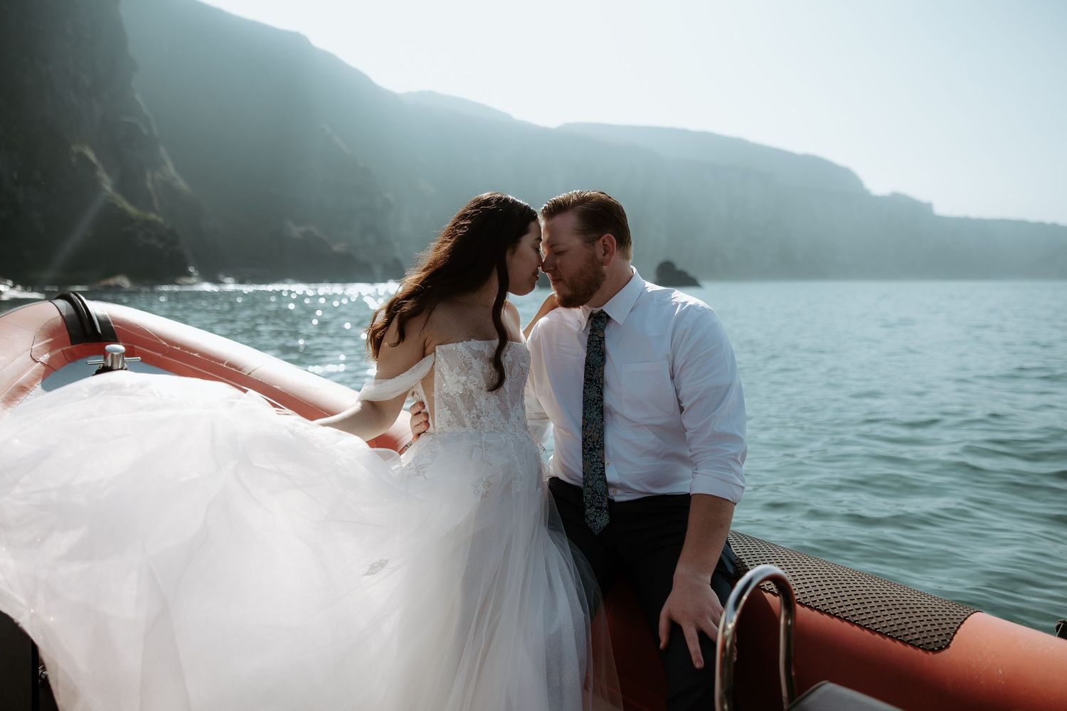 A romantic wedding moment captured on a boat with dramatic coastal cliffs in the background.