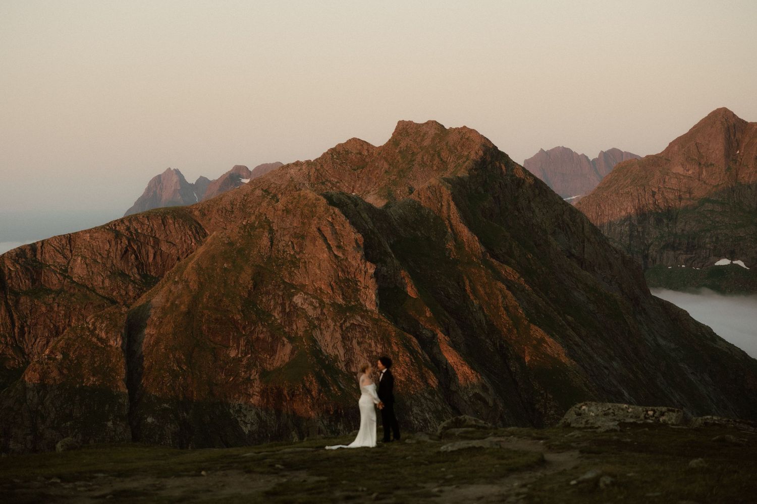 Panoramic view of rocky mountain ridges against a soft sunset sky over coastal waters.