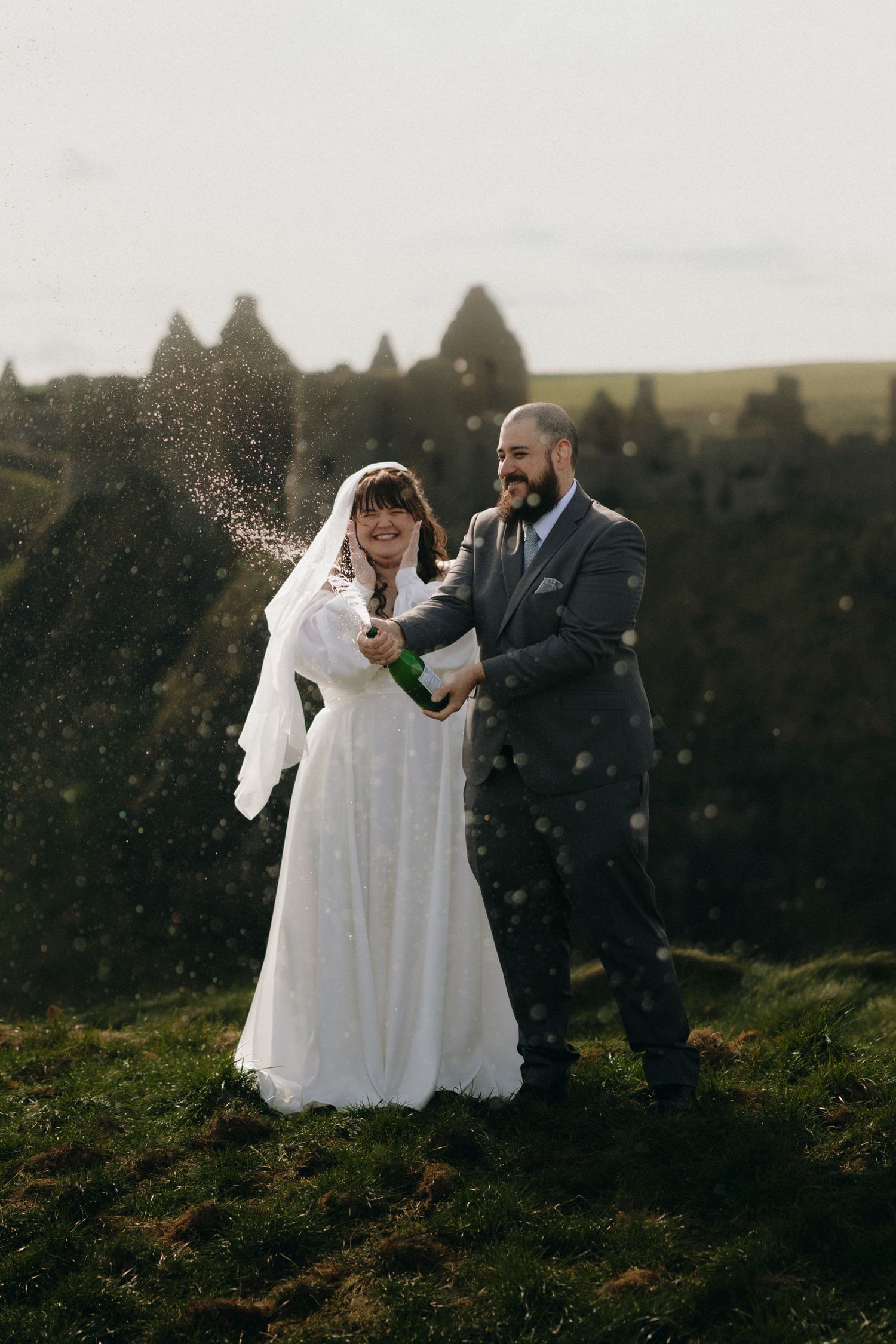 Couple celebrates in formal attire on misty hillside during outdoor photoshoot.