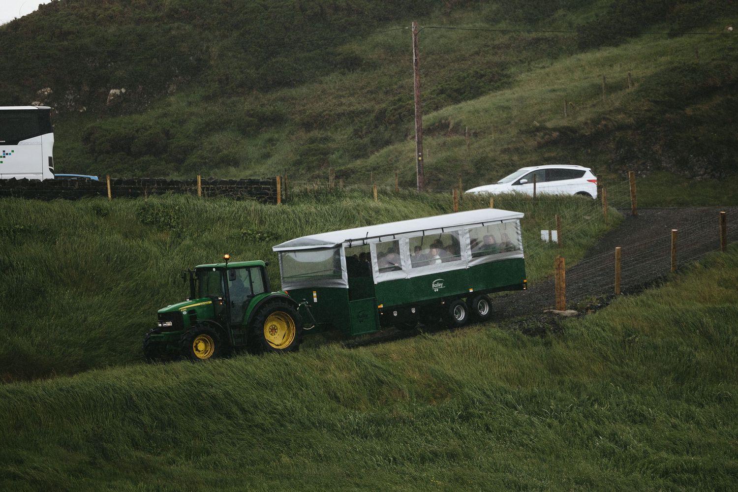 A green John Deere tractor and white shuttle bus are parked on a grassy hillside.