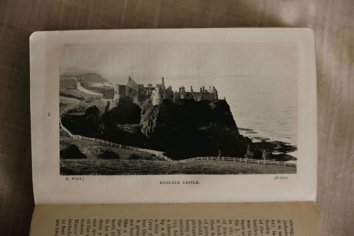 Vintage black and white photograph of Dunluce Castle perched on rocky cliffs in Northern Ireland, featured in an old book.