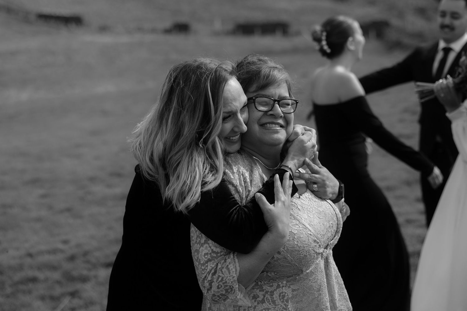 A joyful embrace shared between guests at an outdoor wedding celebration, captured in black and white photography.