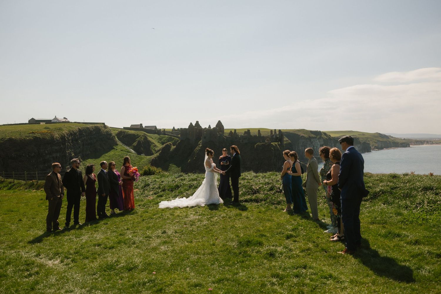 Wedding party gathers on a scenic coastal hillside overlooking the ocean for outdoor ceremony photos.