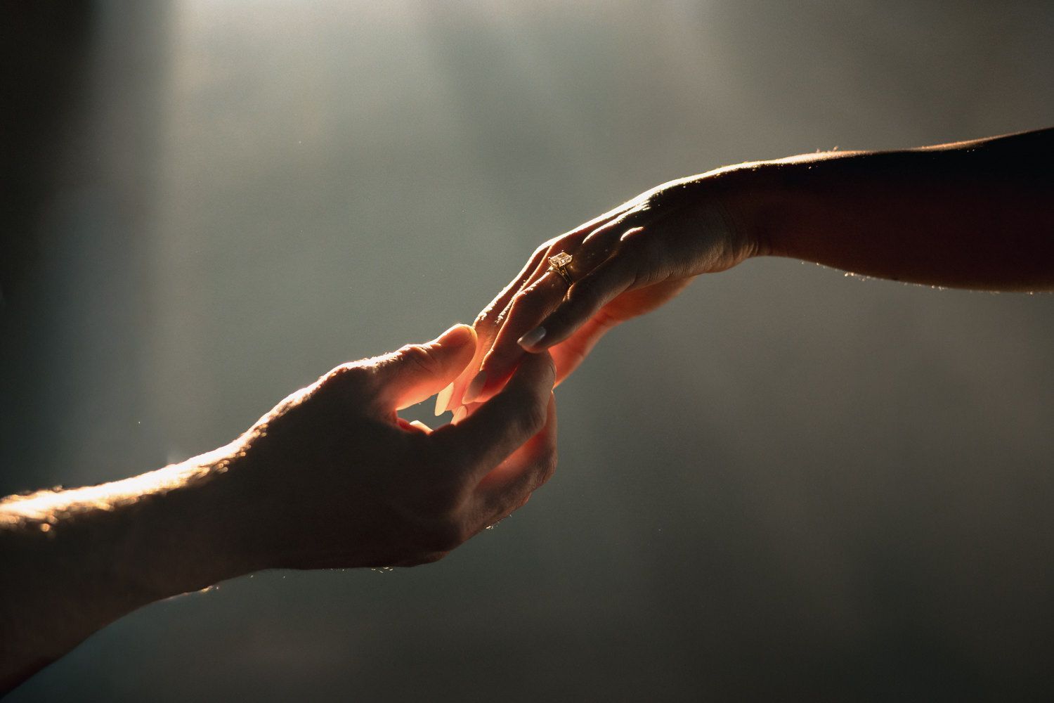 Dramatic backlit hands reach across a moody dark background.