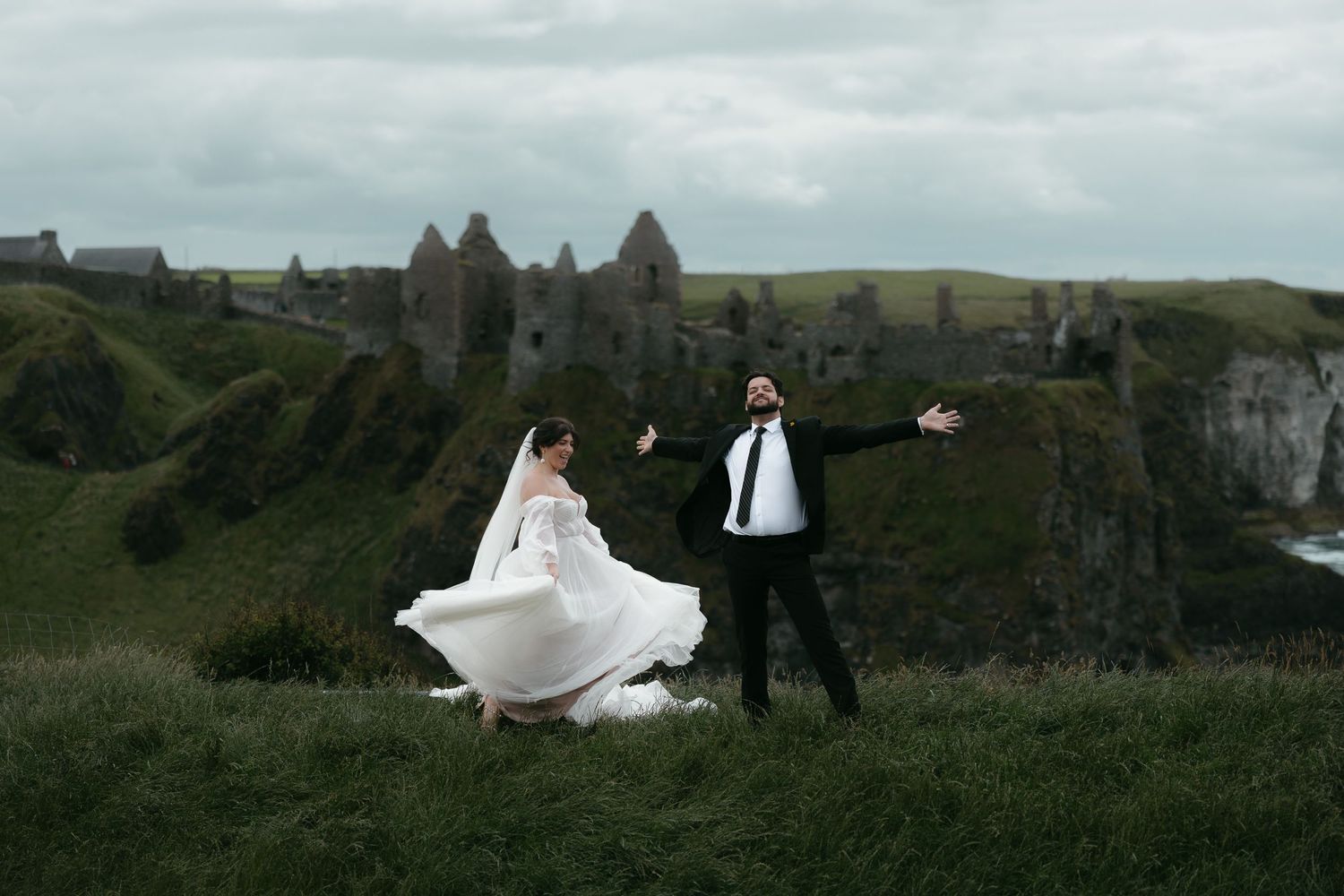 Couple dances on green hilltop with ancient castle ruins in background.