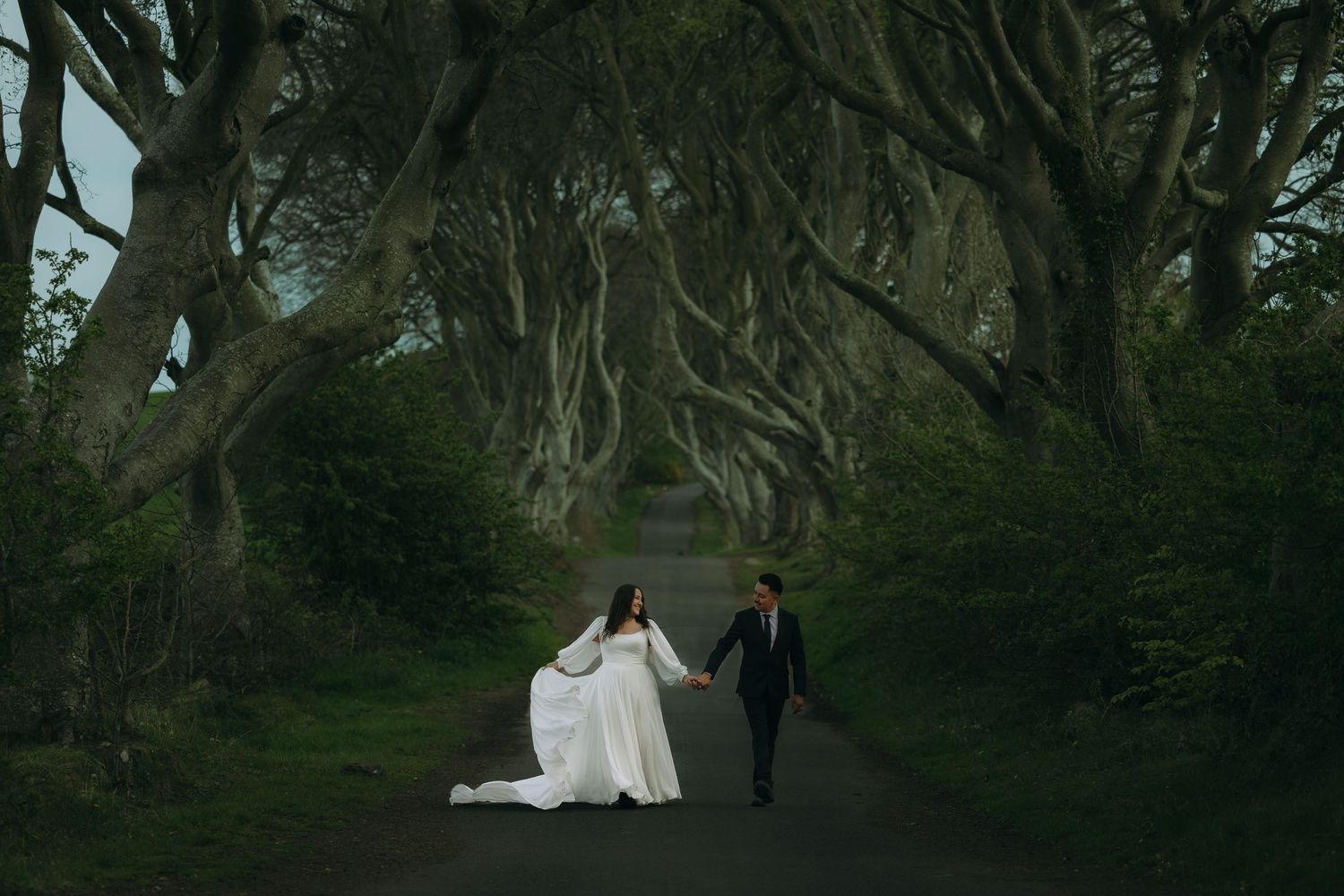 Newlyweds standing beneath a dramatic tree-lined avenue known as the Dark Hedges in Northern Ireland.
