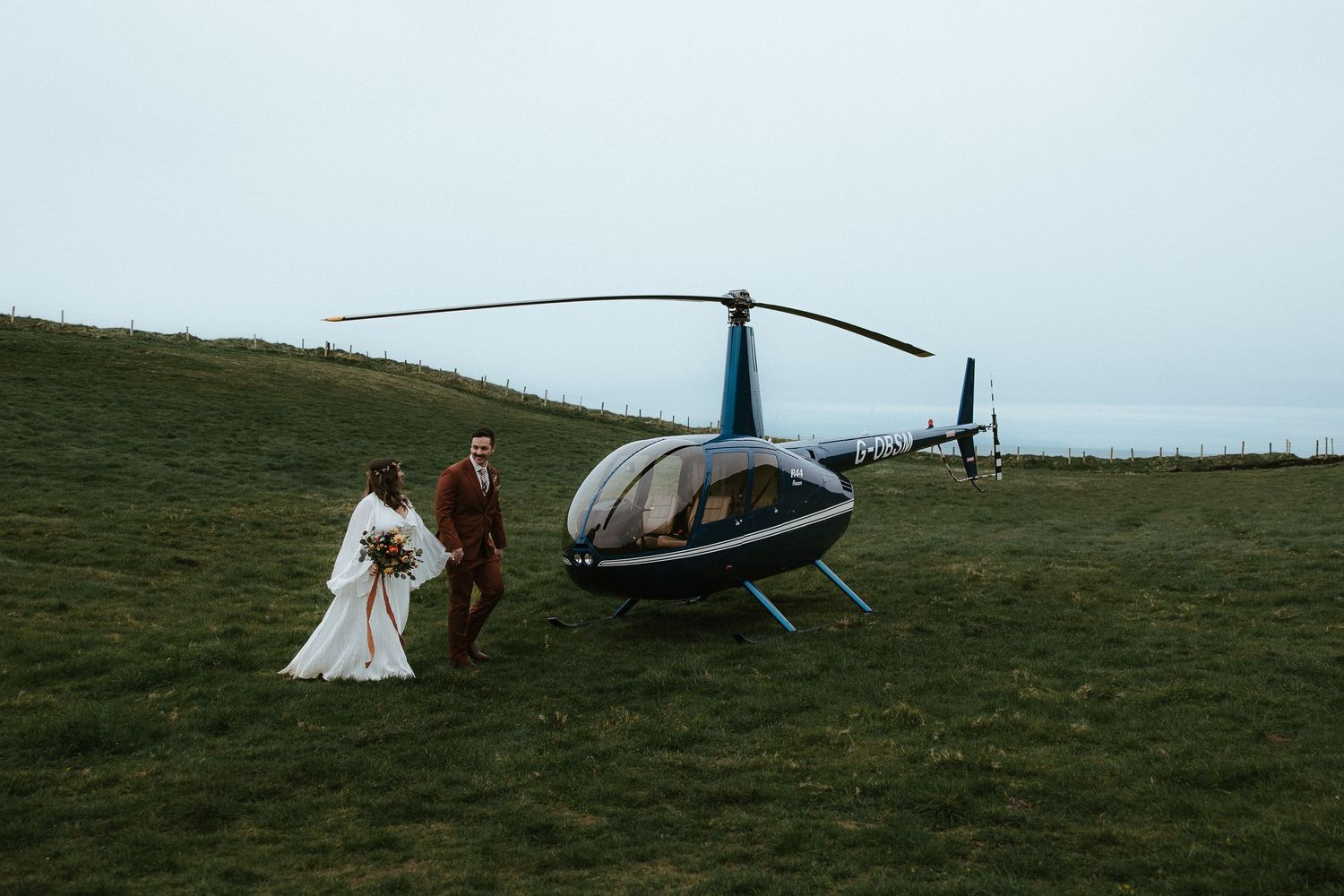 A blue helicopter rests on a grassy hilltop during a wedding photoshoot.
