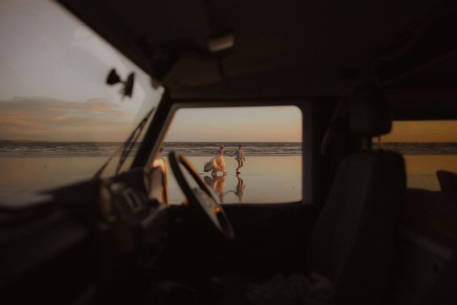 Dark silhouettes against a dramatic sunset beach scene viewed through a car window.