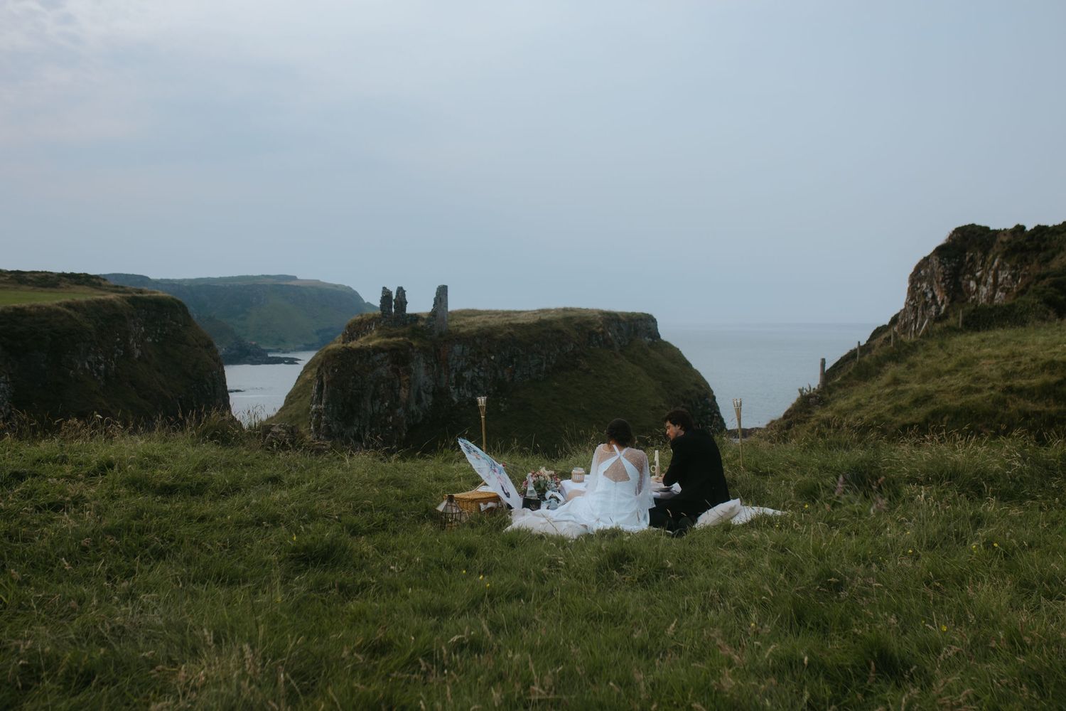 A couple enjoys a coastal picnic on rolling green cliffs by the sea.